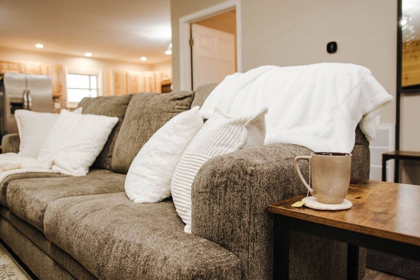 Un salon avec un canapé, des coussins et une table sur laquelle se trouve une tasse.