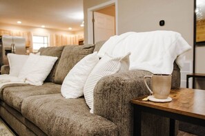 Un salon chaleureux avec un canapé d’angle, une table basse et une porte donnant sur une autre pièce.