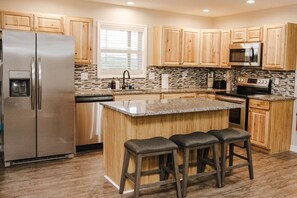 A modern kitchen with a central island, stainless steel appliances, wooden cabinets, and a window providing natural light.