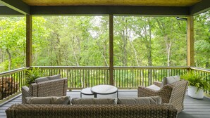 Un espacio de estar al aire libre cubierto, con mobiliario de mimbre y vistas a un bosque.