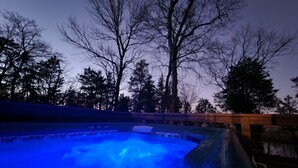 Un jacuzzi con luz azul, rodeado de árboles y una terraza de madera.