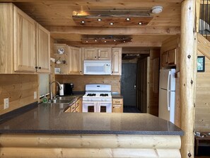 A wooden cabin-style kitchen with a granite countertop, white appliances, and a wooden ceiling. - Cozy Cabin nestled in the woods. Plenty of SNOW MOBILE and ATV PARKING! (Duck Creek Village)