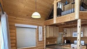 Hirsihirrestä rakennetun mökin sisätilat, joihin kuuluu ruokailutila, keittiö ja parvelle sijoitettu makuuhuone.