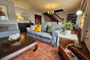 A living room with a grey sofa, a wooden coffee table, a white side table, a potted plant, and a staircase. - 15A04 Duplex and Garage in Downtown by R2R Consulting (Llanes)