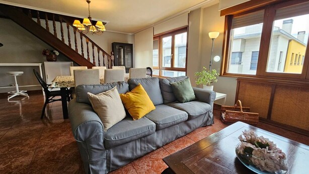 Un salon avec un canapé gris, une table basse, un escalier et une vue sur des immeubles.