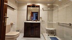 Une salle de bain comprenant des toilettes, un meuble-lavabo avec un miroir, un espace douche et une barre d’appui.