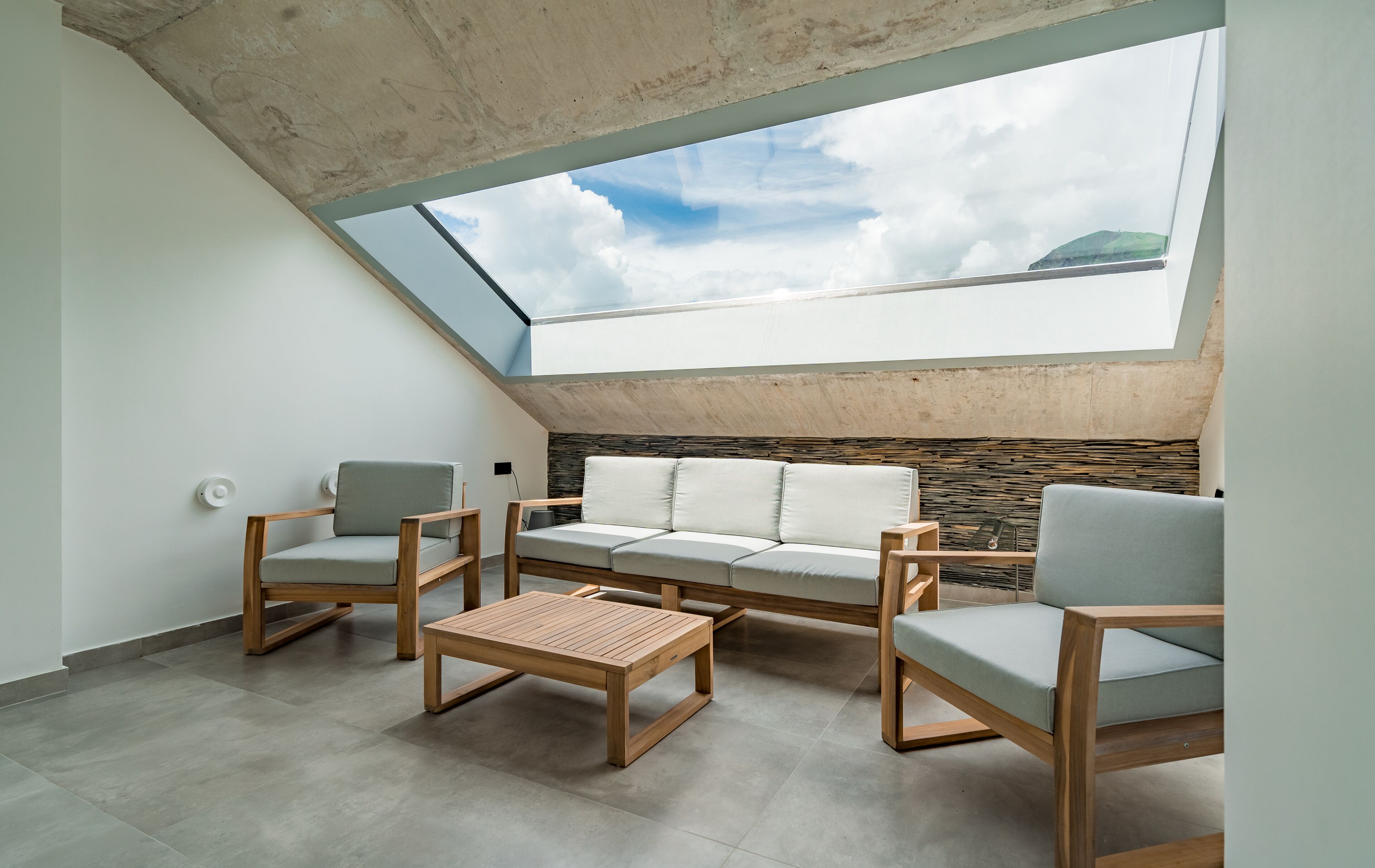 A modern interior with a sloped ceiling, a stone wall, and a large skylight.