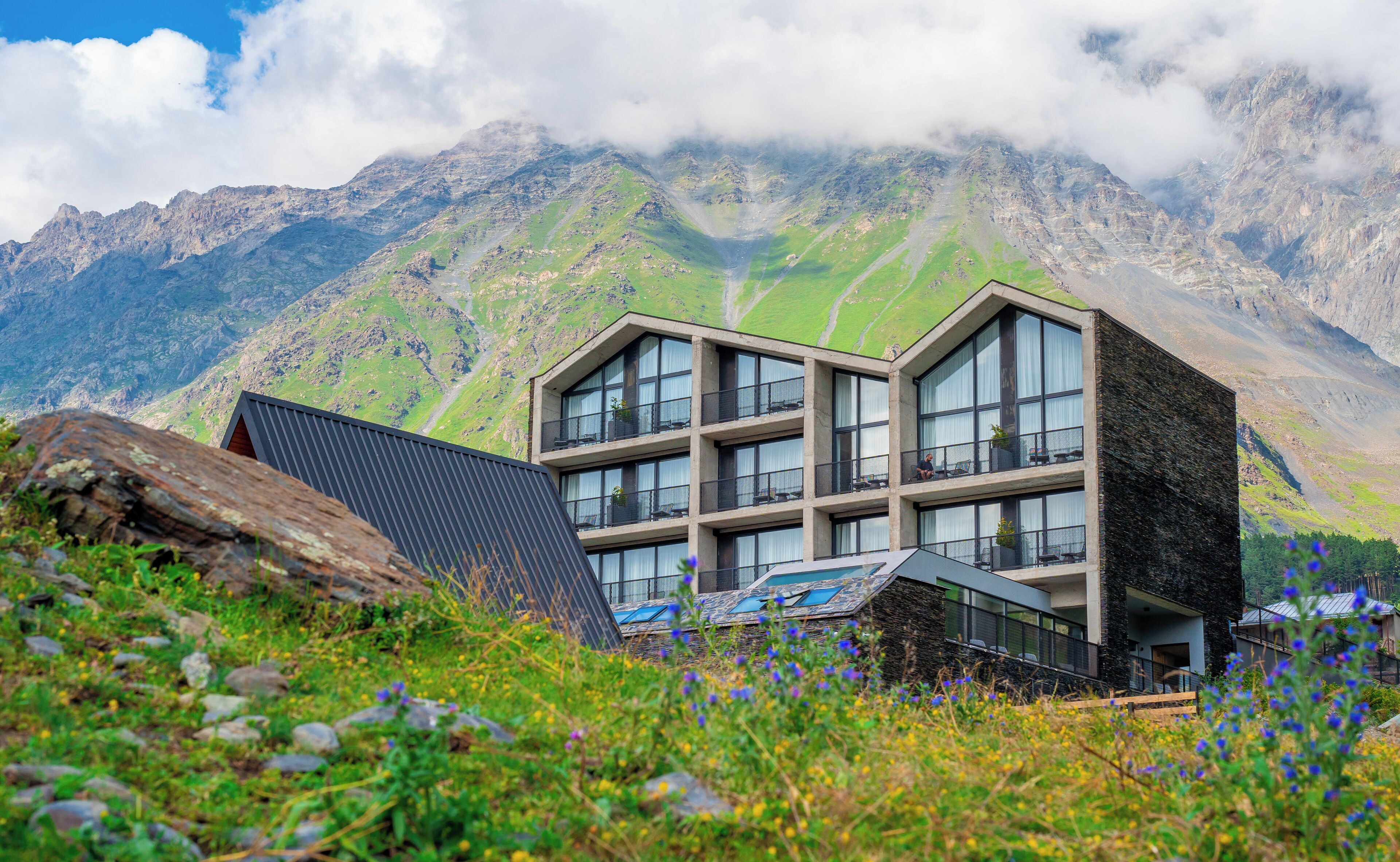 A modern building with multiple balconies, surrounded by a mountainous landscape.