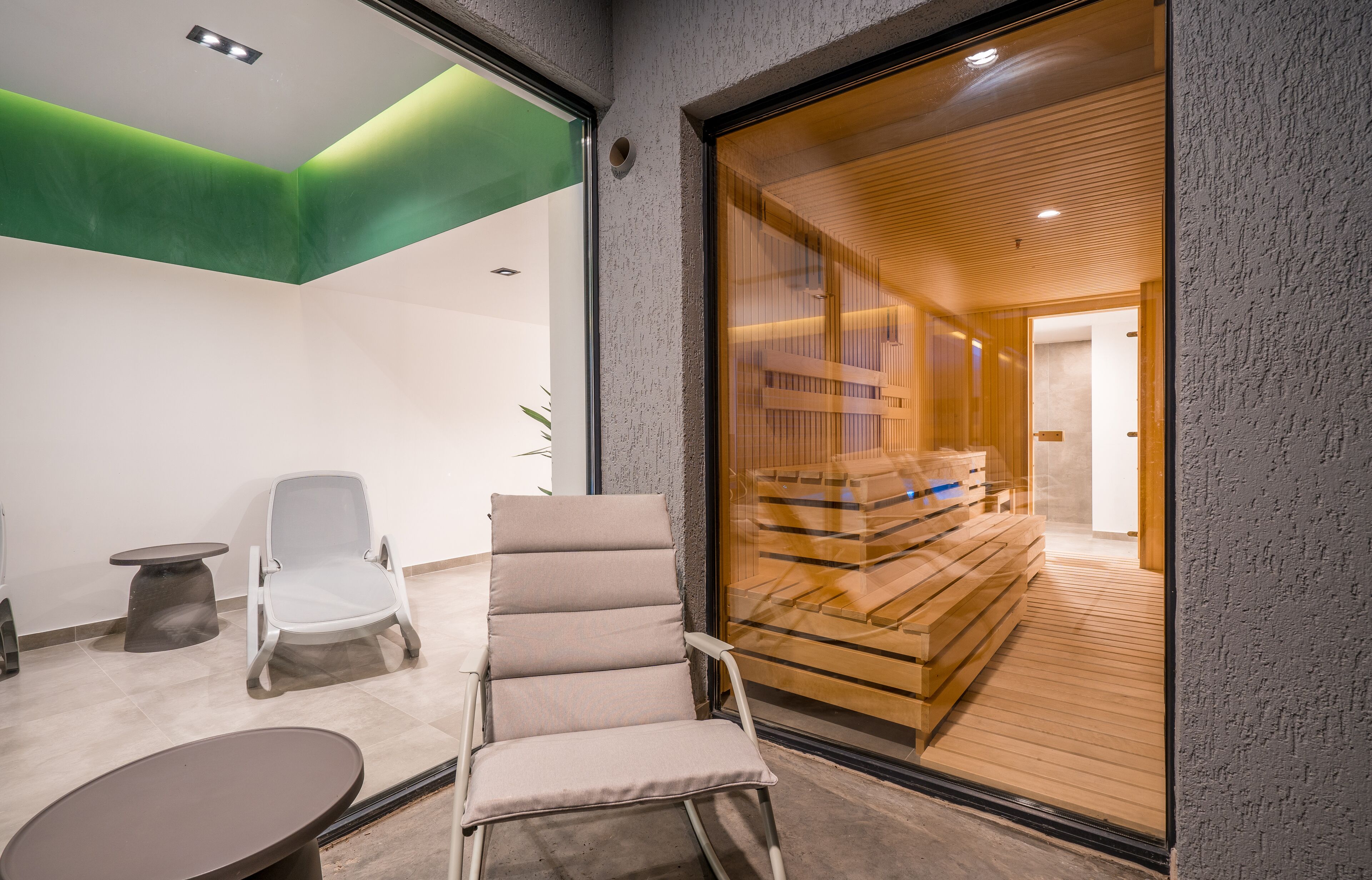 Un interior moderno con una zona de estar, una pared de vidrio que conduce a una habitación de madera y un detalle verde en el techo.