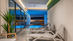 Un área interior de piscina moderna con paredes de vidrio, sillones de descanso y una zona de estar con mesas.