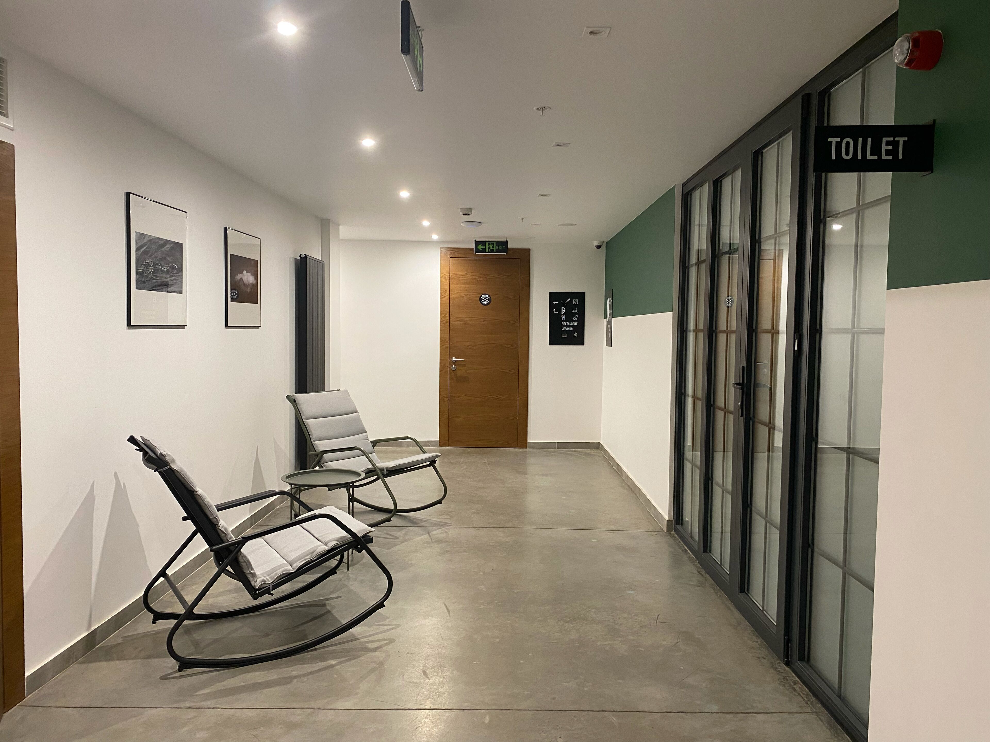 A hallway with two rocking chairs, a wooden door, and a sign indicating a toilet.