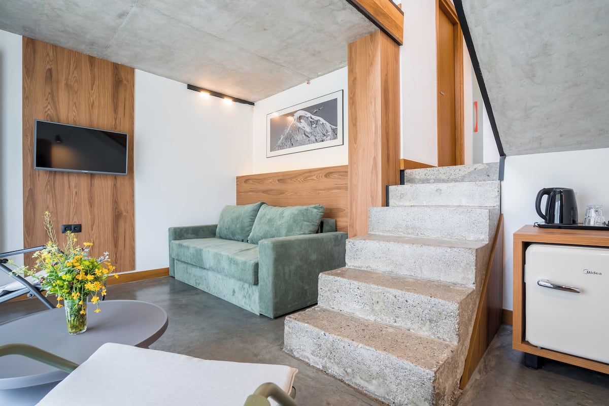 Un espace de vie moderne avec un canapé vert, une tête de lit en bois, un escalier et un coin cuisine.