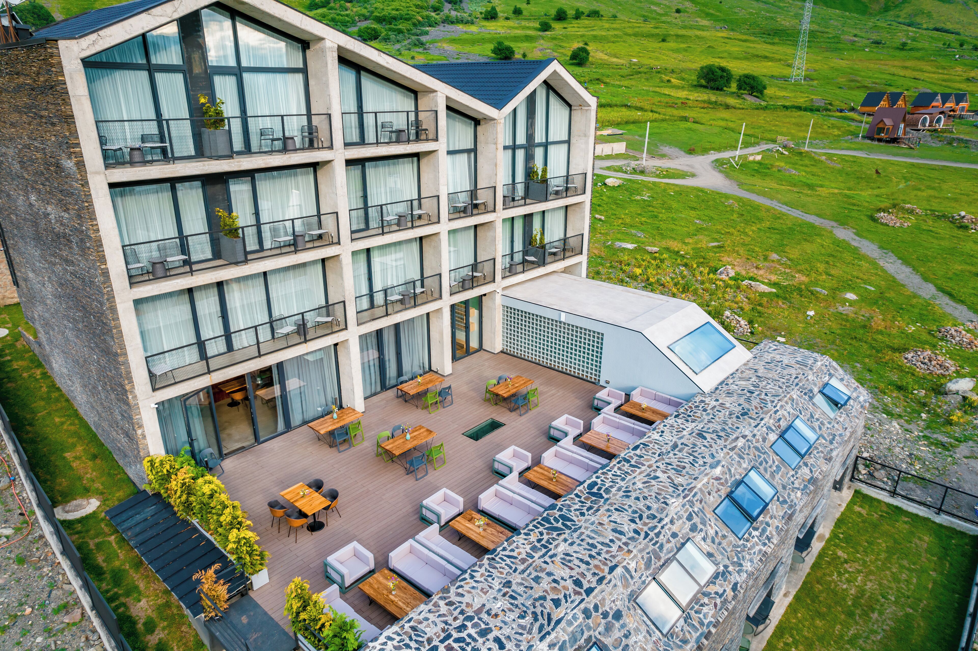 A modern hotel with multiple balconies, outdoor seating, and a stone facade.