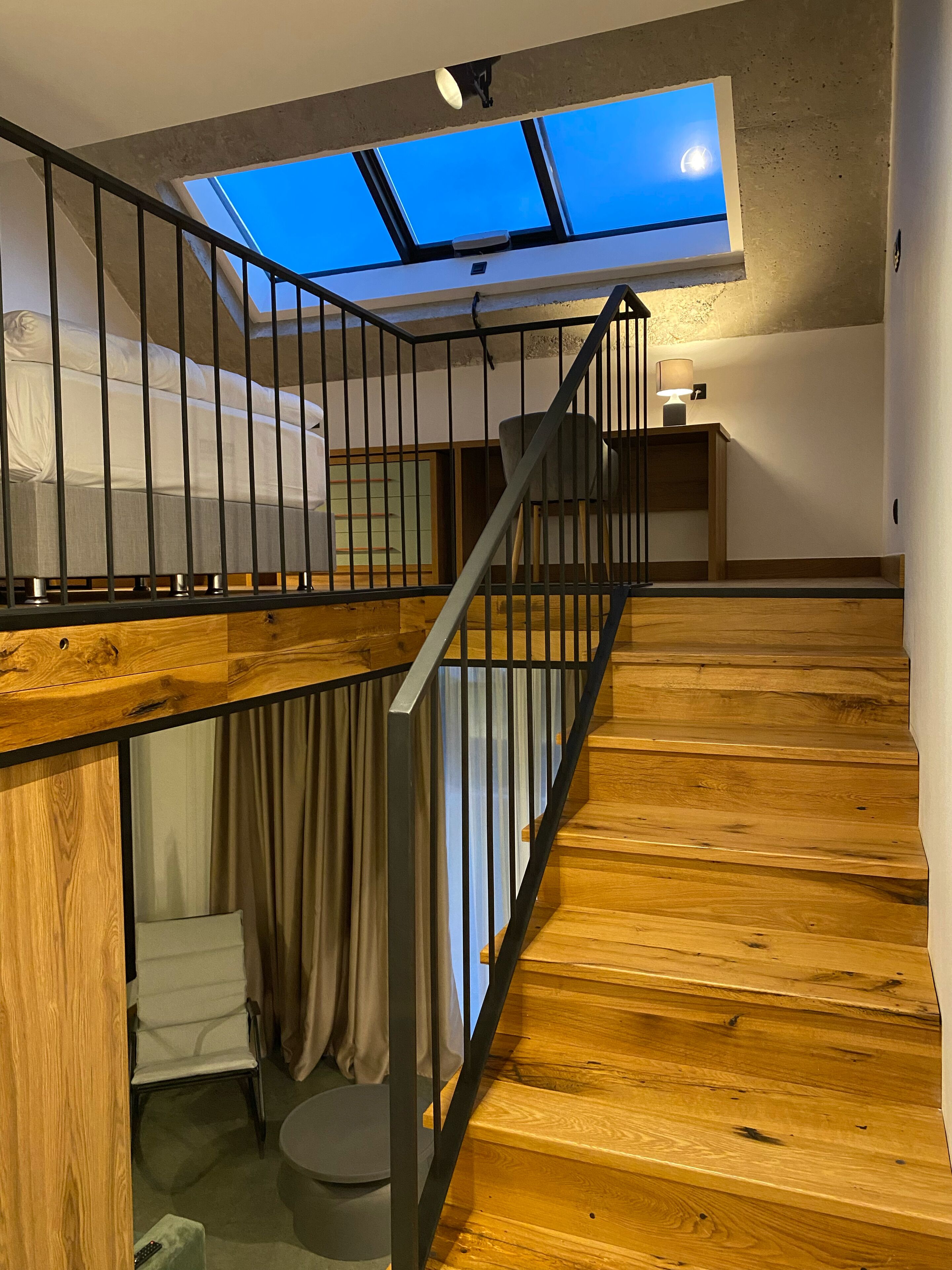 Un dormitorio tipo loft con tragaluces, escalera de madera y un baño pequeño.