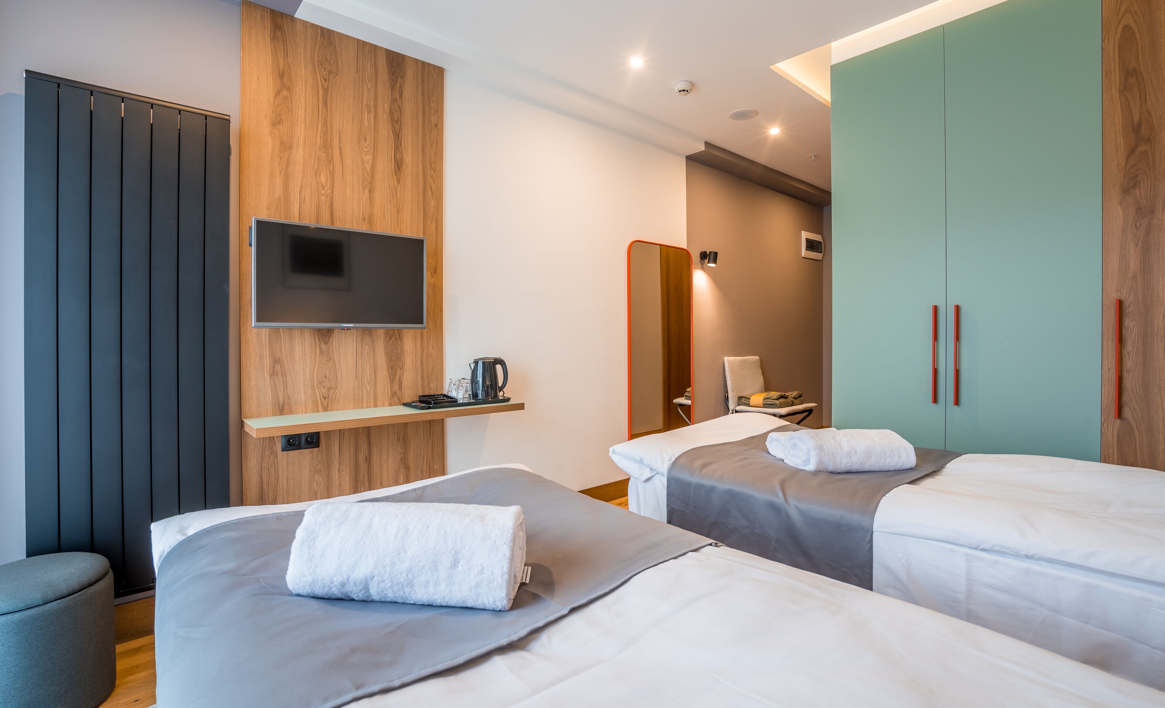 Habitación de hotel con dos camas, un televisor montado en un panel de madera, un espejo y un armario.
