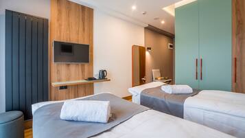 Habitación de hotel con dos camas, un televisor montado en un panel de madera, un espejo y un armario.