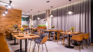 Interior de restaurante con mesas de madera, sillas negras e iluminación colgante.