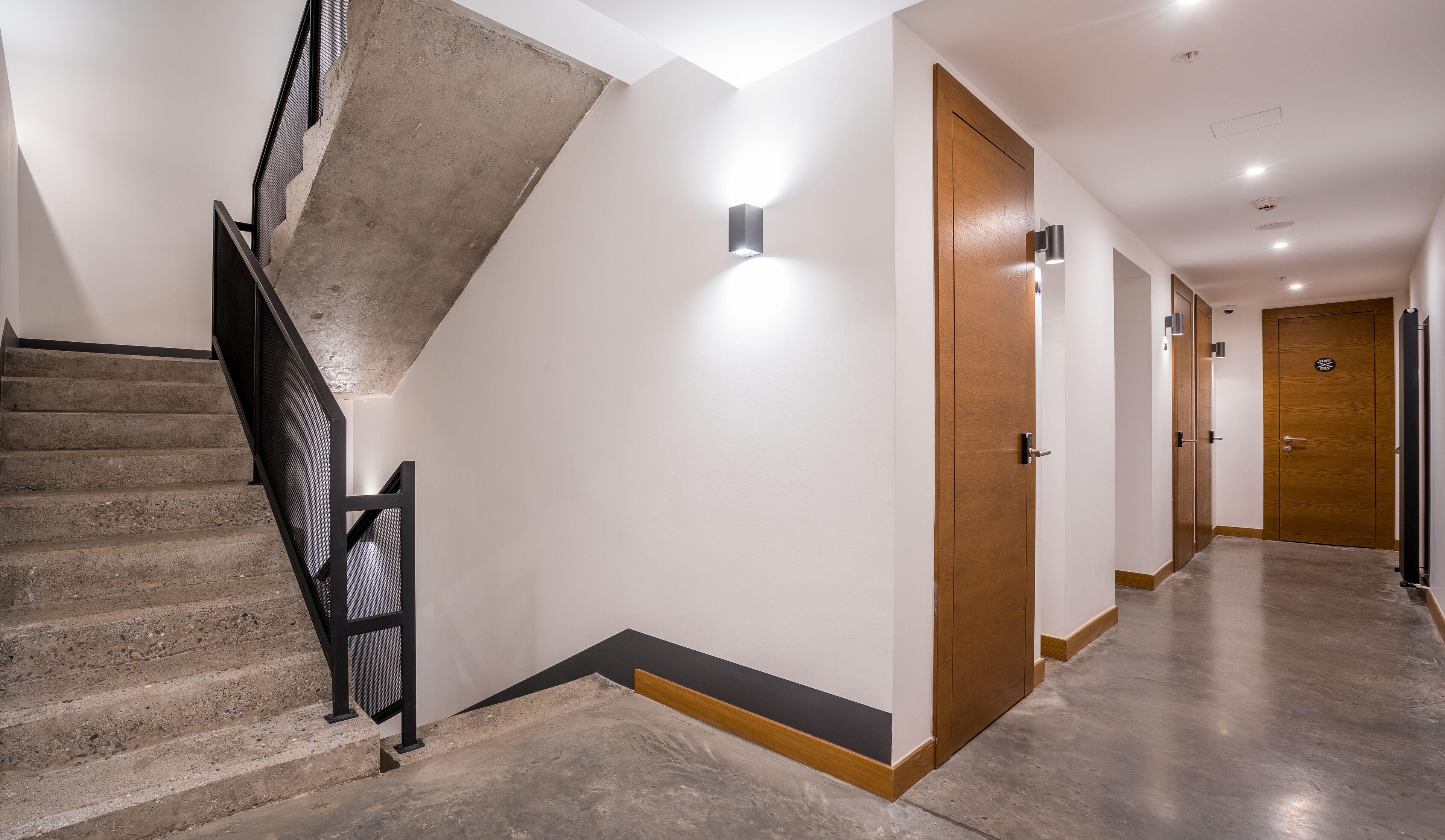 Un intérieur moderne avec un escalier en béton, une porte en bois et un couloir doté d’un éclairage encastré.