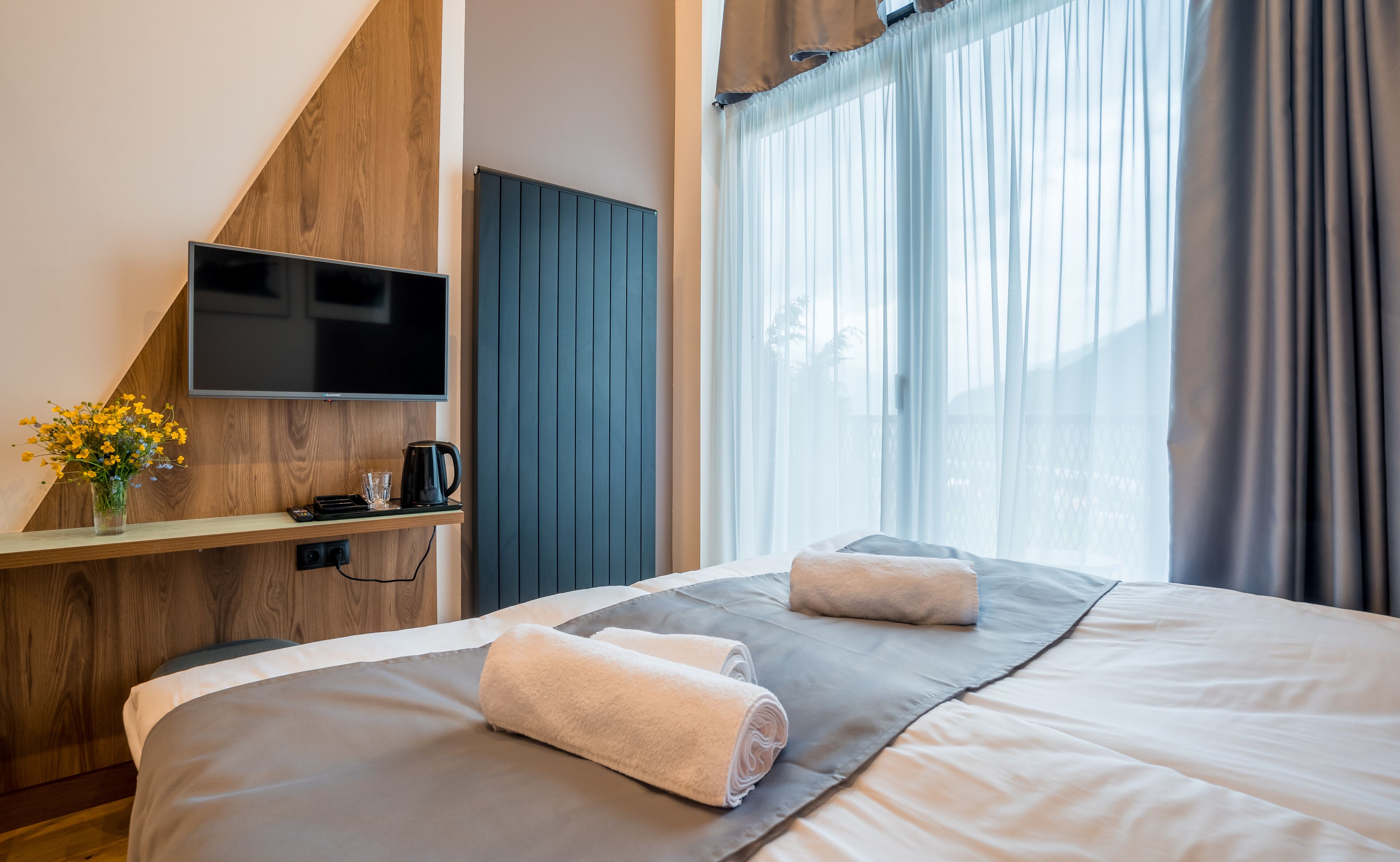 Une chambre d’hôtel avec un lit, un téléviseur fixé au mur en bois, une machine à café et une fenêtre avec des rideaux.