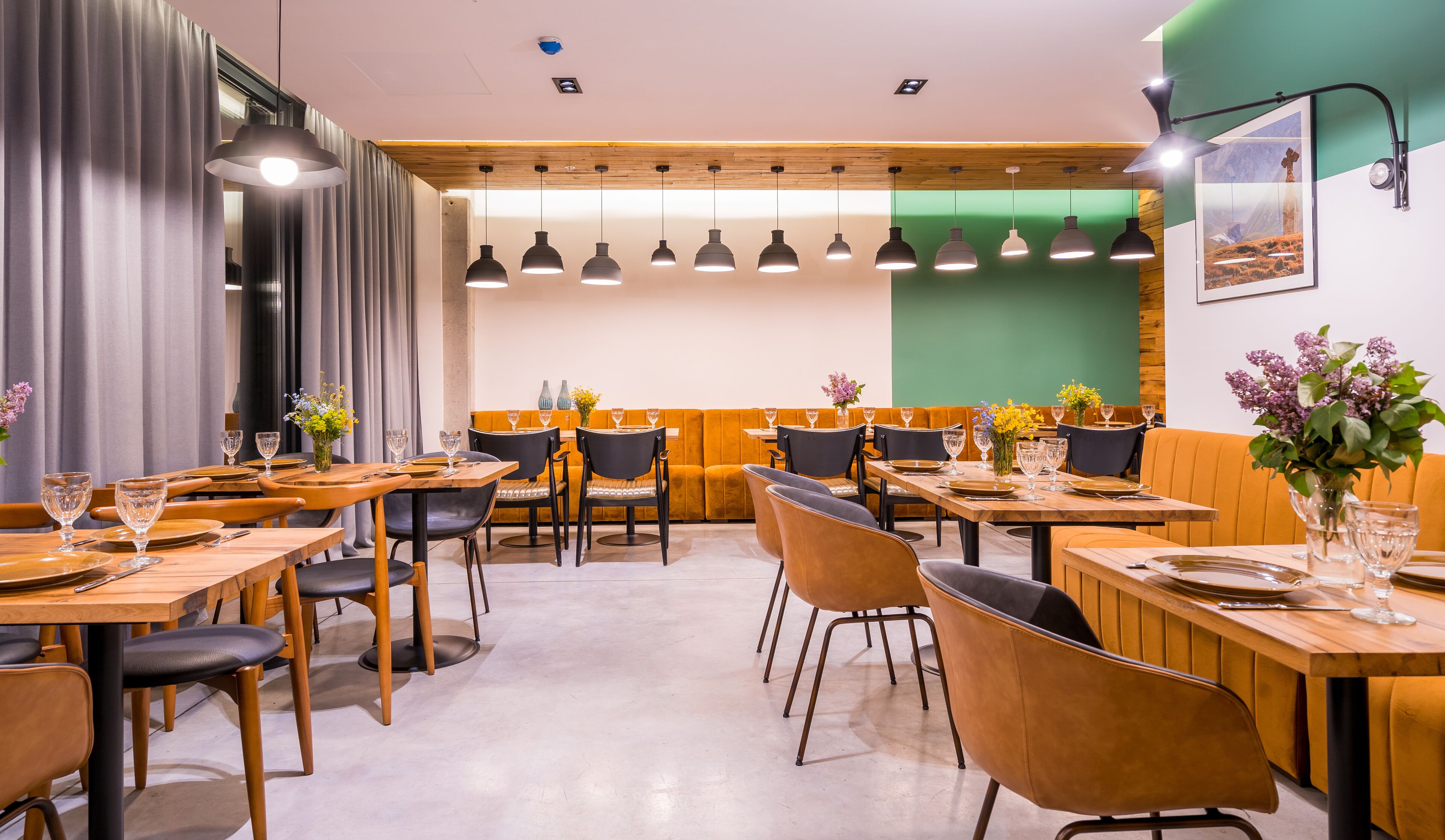 A restaurant with wooden tables and chairs, a green accent wall, and pendant lighting.