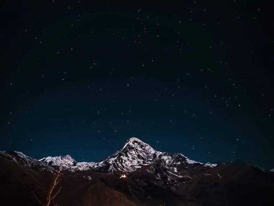 A mountain with a snow-capped peak under a starry night sky.
