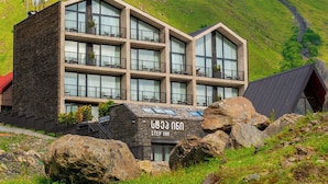 Un hotel moderno con fachada de piedra y varios balcones, con montañas al fondo.