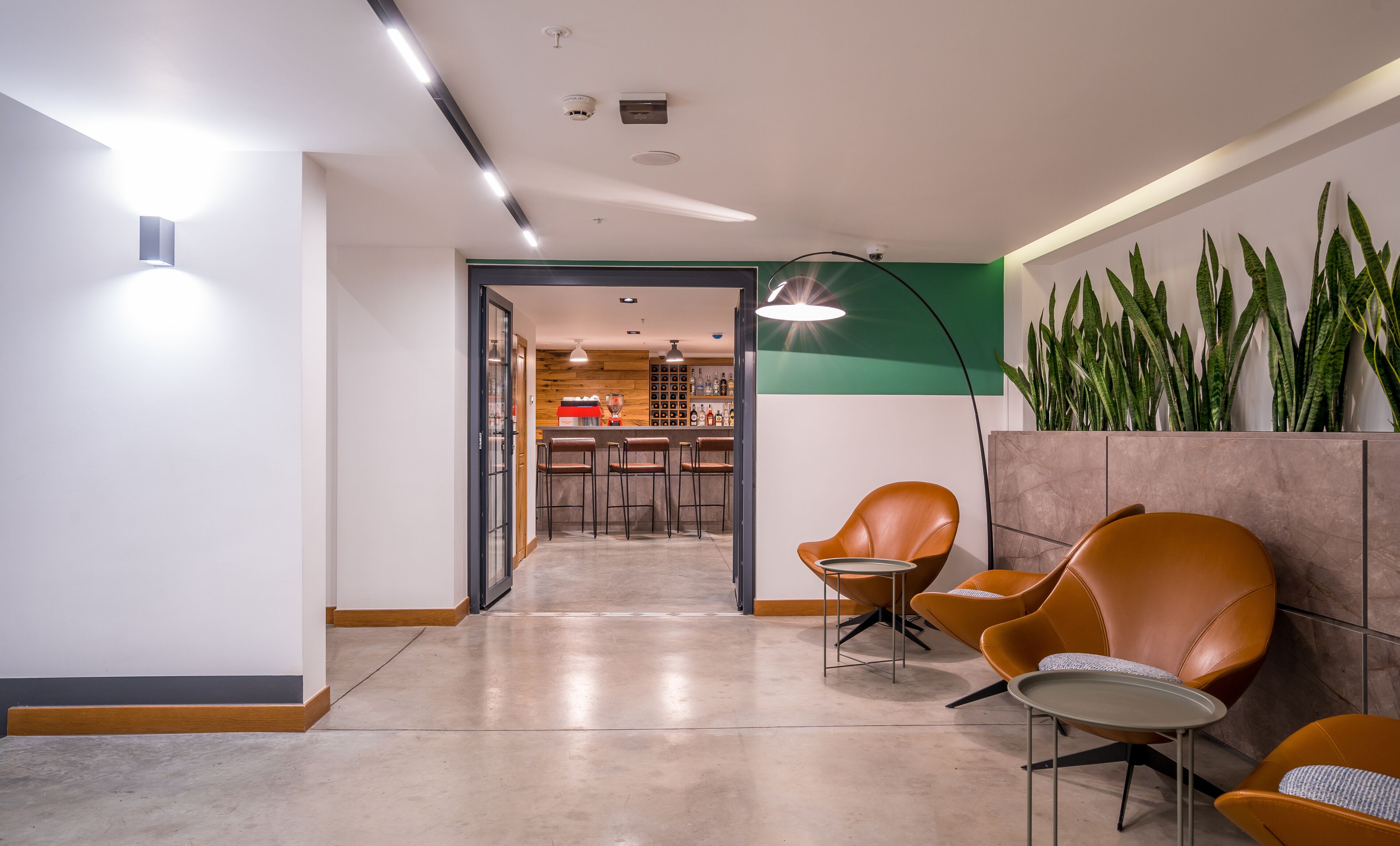 Un vestíbulo moderno con zona de bar, sillones de cuero y una pared decorada en tonos verdes.