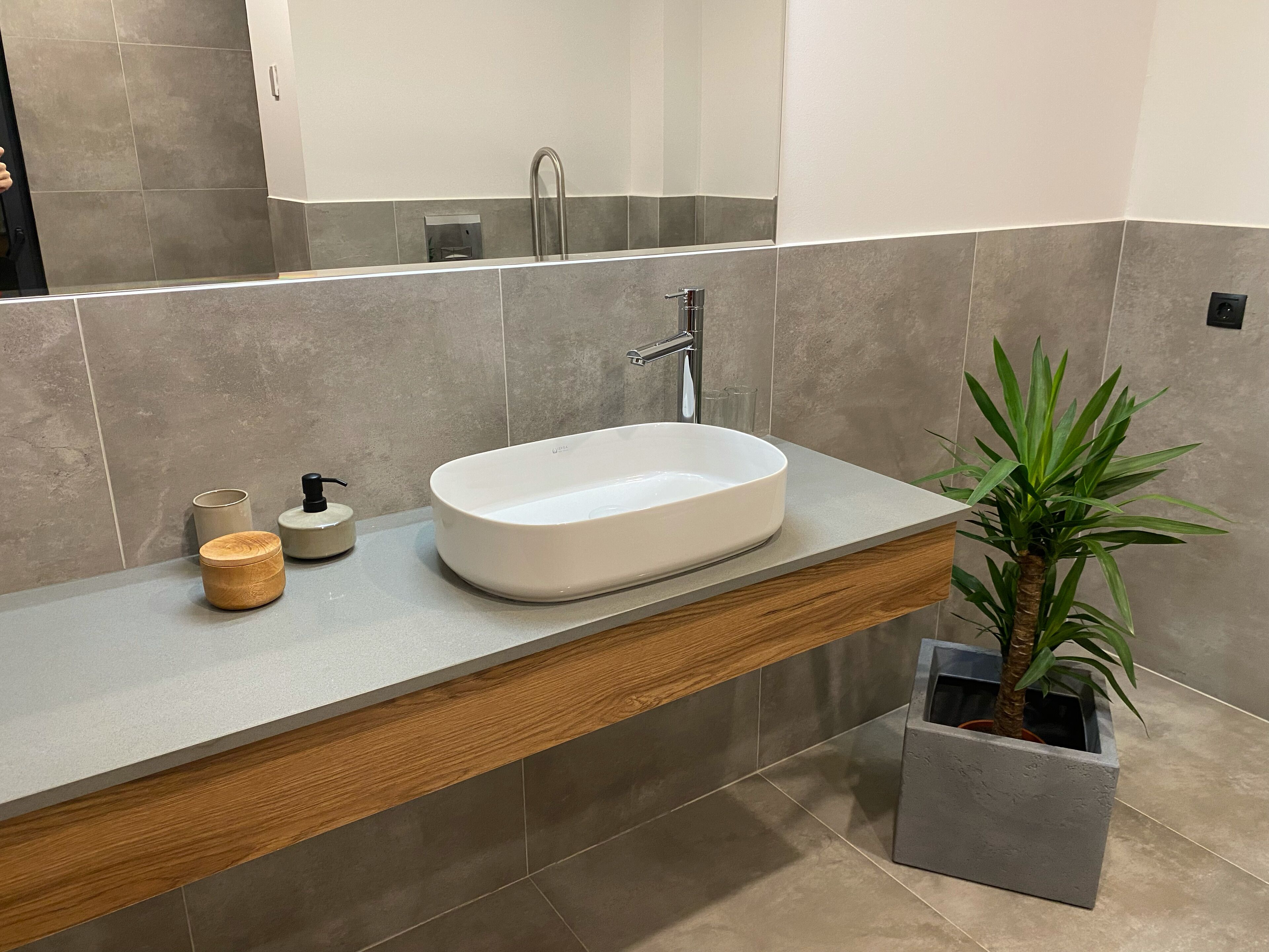 A modern bathroom with a built-in sink, a wooden vanity, a mirror, and a potted plant.