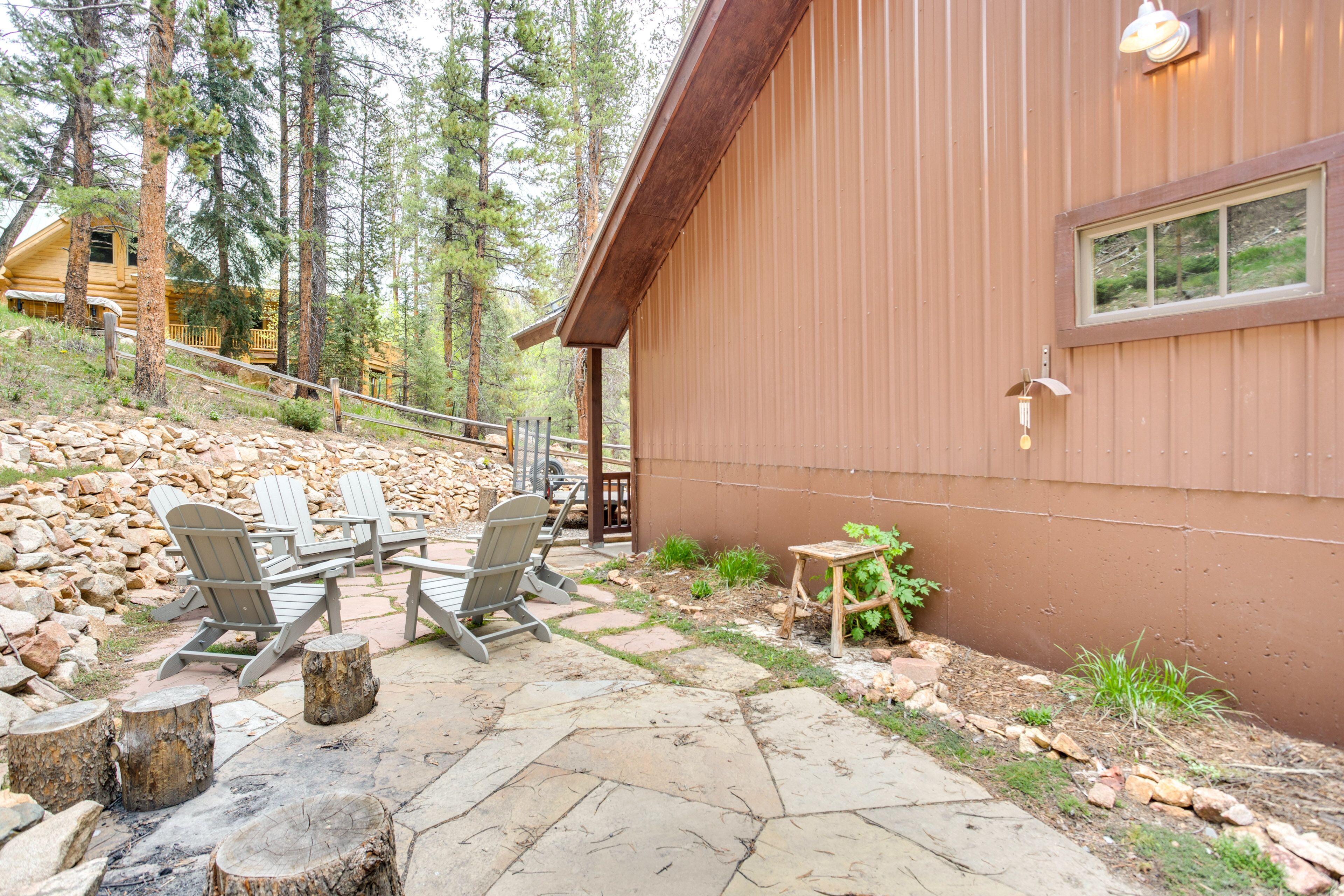 Een houten chalet met een stenen terras, Adirondack-stoelen en een kleine tafel.