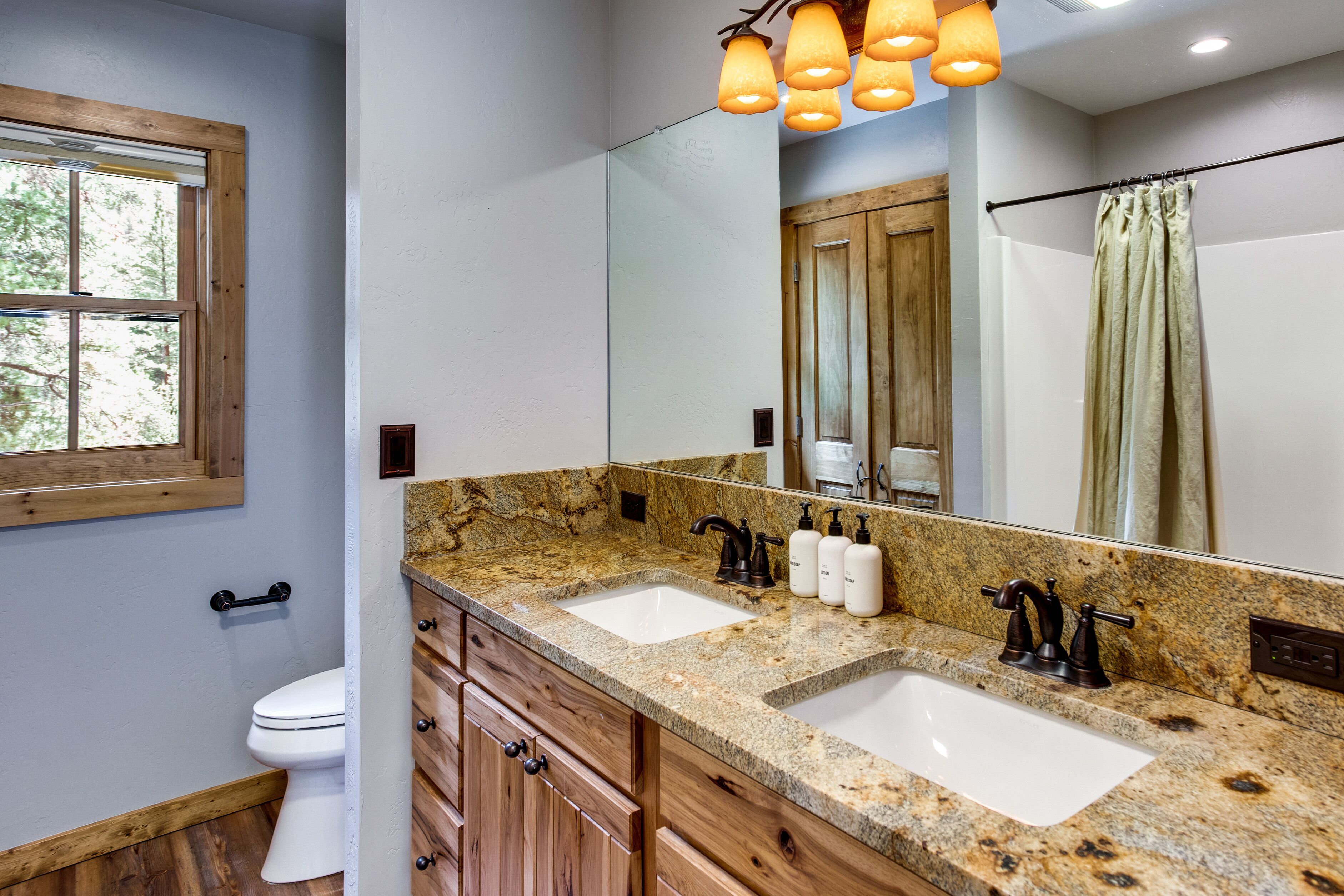 A bathroom with two sinks, wooden cabinets, a large mirror, and a window.