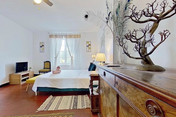 Habitación de hotel con una cama, un aparador de madera, un televisor, una lámpara y una planta decorativa.