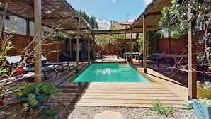 A pool area with wooden decking, lounge chairs, and potted plants.