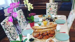 A dining table set with plates, bread, pastries, fruits, and a knife.