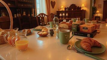 A breakfast table with croissants, bread, a croissant on a plate, a green mug, a glass of orange juice, and a bottle of water.