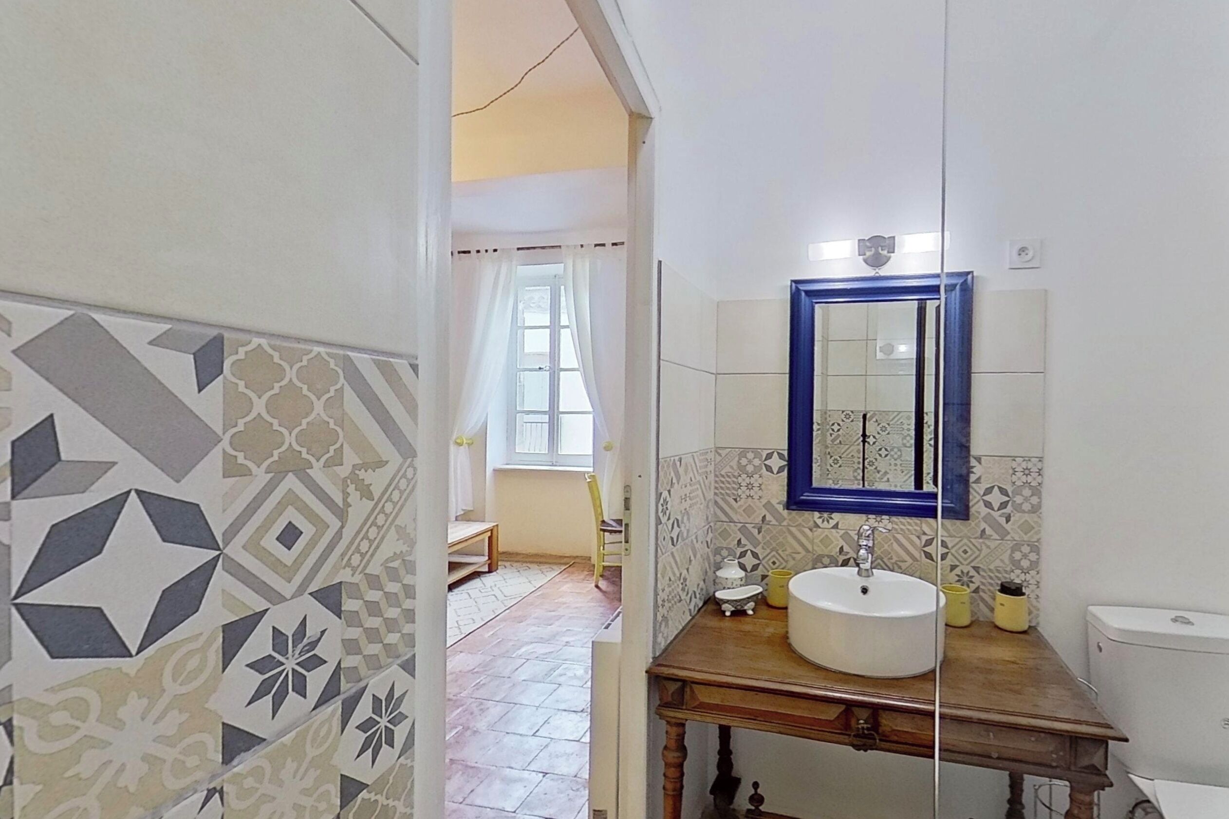 Un bagno con un lavandino bianco, uno specchio con cornice blu e piastrelle decorate.