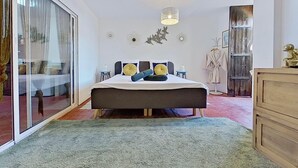 A bedroom with a large bed, a sliding glass door, a wooden wardrobe, and a hanging light fixture.