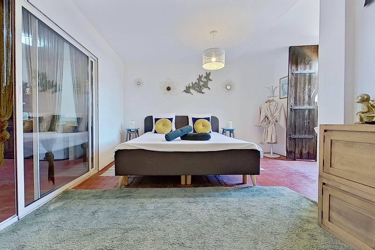 A bedroom with a large bed, a sliding glass door, a wooden wardrobe, and a hanging light fixture.
