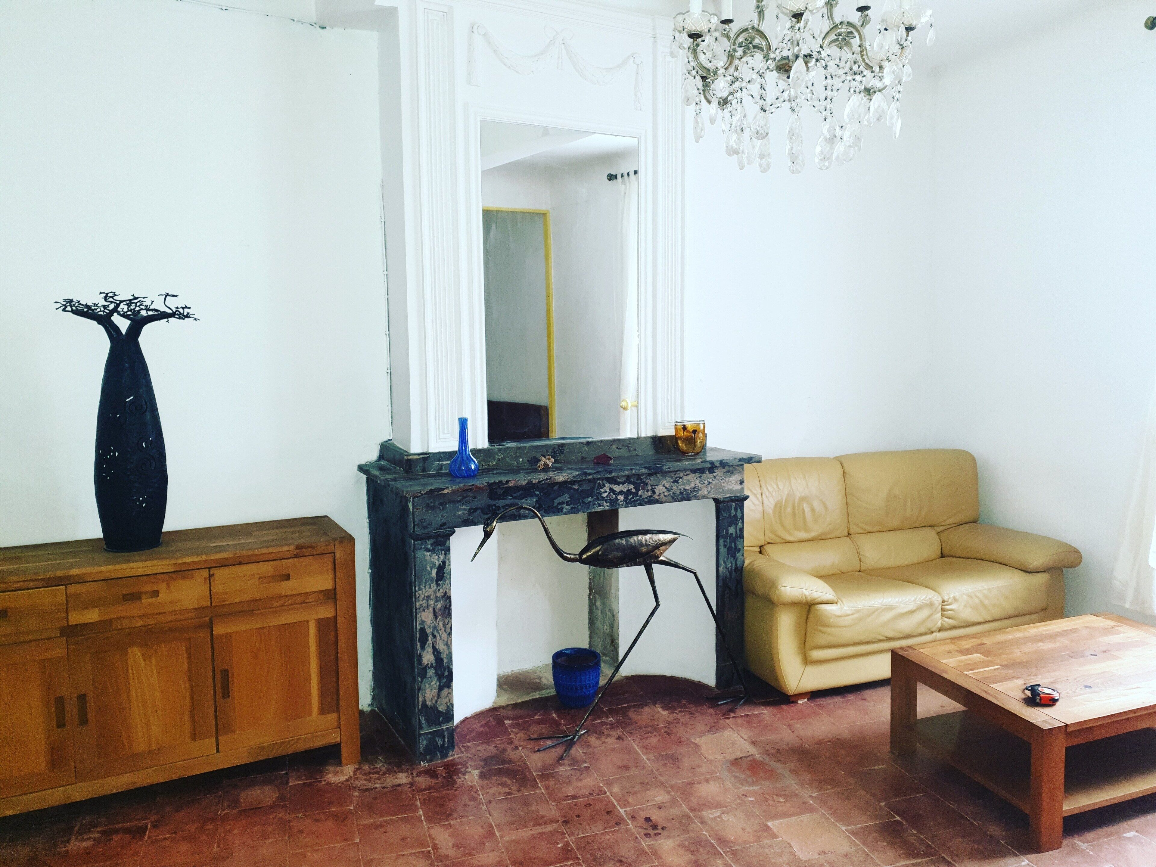 Un salon avec un meuble en bois, un vase bleu, un canapé jaune, une table basse en bois et un lustre.