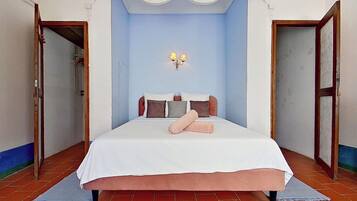 Un dormitorio con una cama grande, una mesita de noche, una lámpara de pared y una puerta que da a otra habitación.