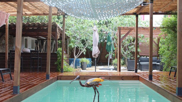 A pool area with a wooden deck, a pergola with a patterned canopy, and a dining area with outdoor furniture.
