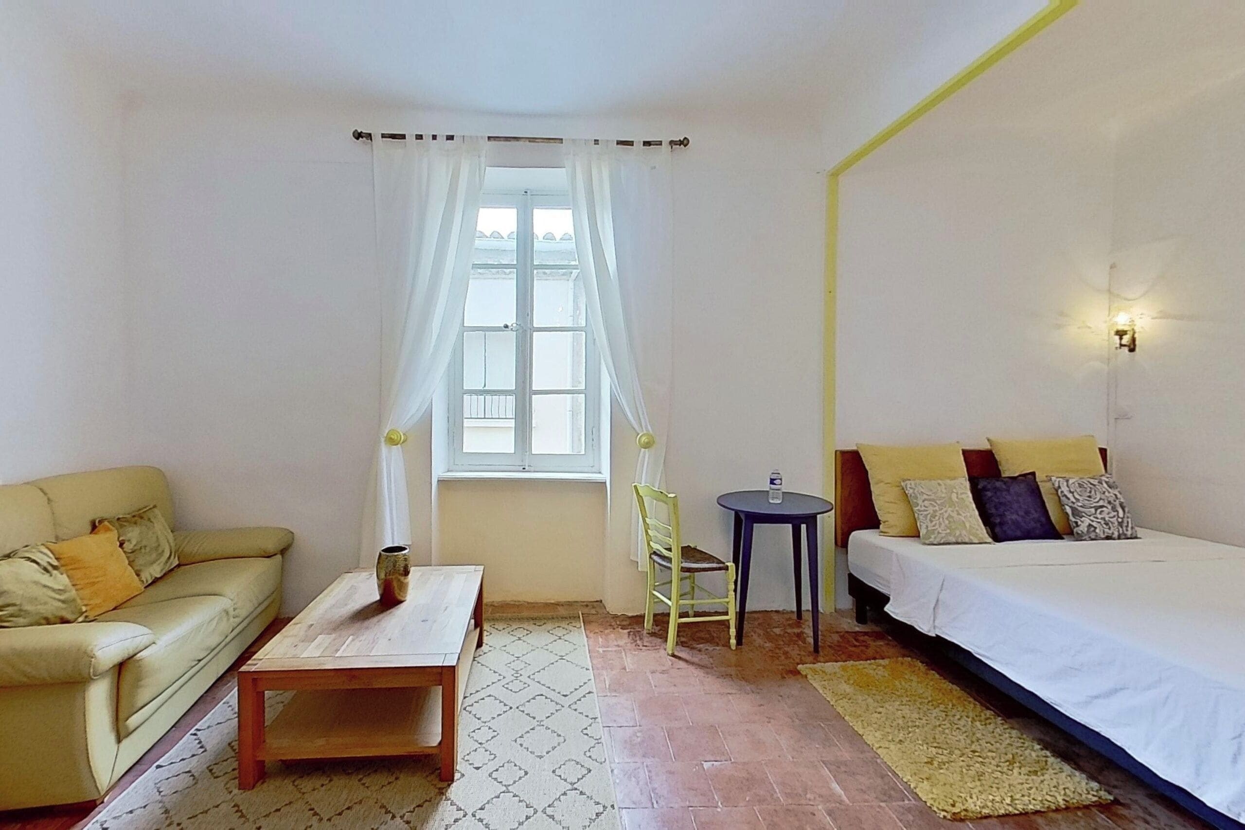 A room with a bed, a sofa, a small table, a chair, and a window with curtains.