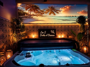 Un área de spa con una bañera de hidromasaje, un mural de playa tropical y un cartel que dice 'Les 2 Drôles d'Oiseaux'.