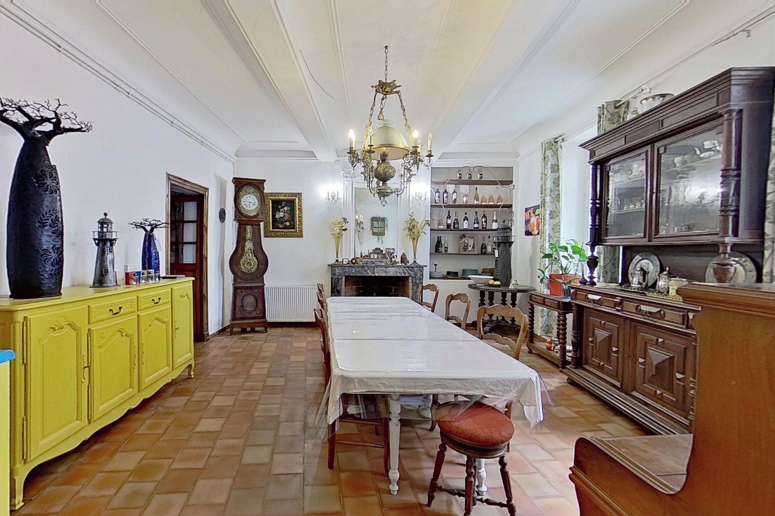 Un coin repas avec une longue table, des meubles de rangement jaunes, un lustre et un meuble à bouteilles.