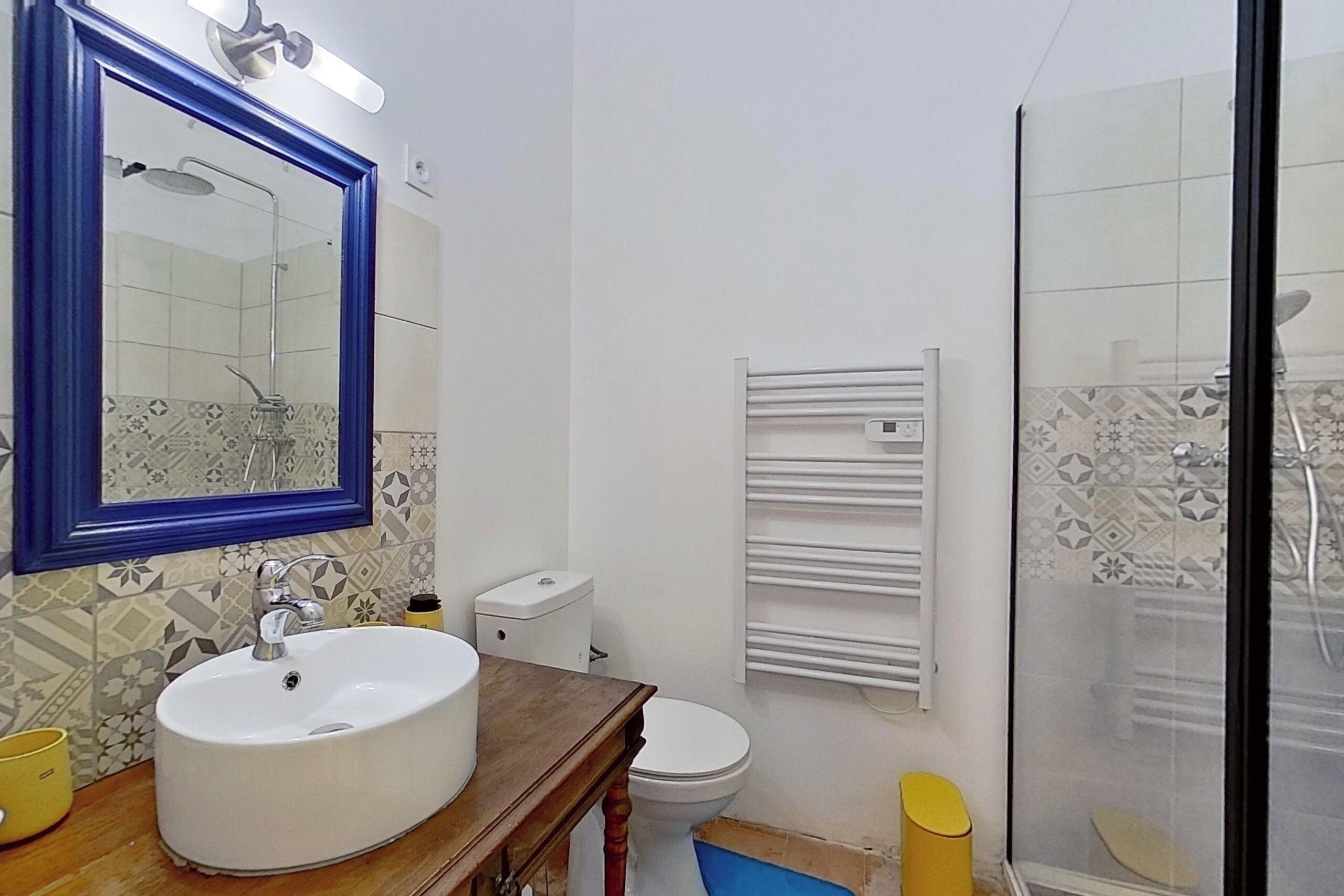 A bathroom with a white sink, a mirror with a blue frame, a toilet, and a shower enclosure.