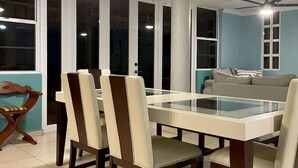 A dining area with a glass-top table and four chairs, a ceiling fan, and a sofa in the background. - #25 5,000 SqFt Penthouse w/ Private Rooftop Loft (Cabo Rojo)
