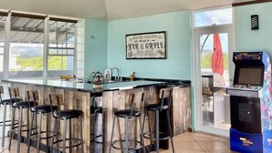 A bar area with a wooden bar counter, bar stools, a vintage sign, and a gaming machine. - #25 5,000 SqFt Penthouse w/ Private Rooftop Loft (Cabo Rojo)