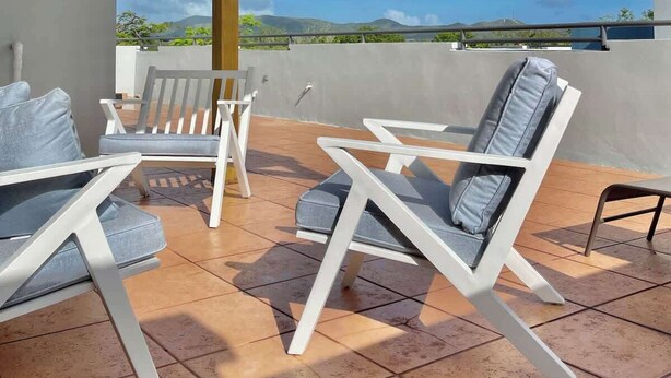 A covered outdoor seating area with white chairs and a table, overlooking a scenic landscape. - #25 5,000 SqFt Penthouse w/ Private Rooftop Loft (Cabo Rojo)