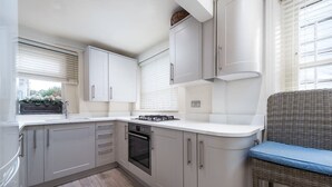 A modern kitchen with grey cabinets, a built-in oven, and a wicker chair with a cushion.