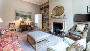 A living room with a fireplace, bookshelves, a television, and a painting on the wall.
