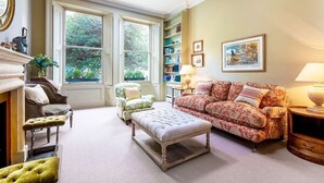 A cozy living room with a fireplace, a large window, a bookshelf, and a patterned sofa.